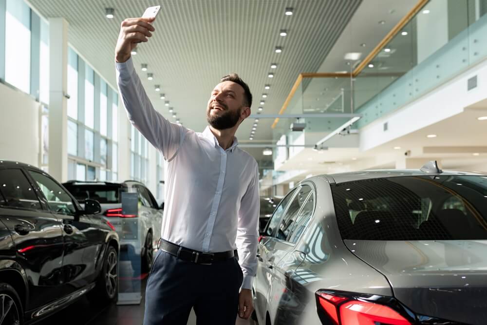 Automobile salesperson recording social media marketing video on showroom floor.