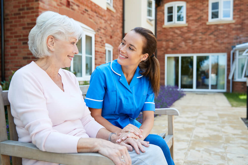 Resident and staff member relaxing outside senior living facility